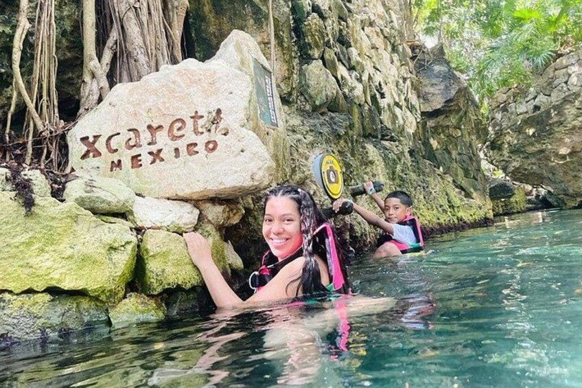 Masa de agua natural con una roca que lleva la inscripción 'Xcaret Mexico' y una persona sosteniendo una pala. 1