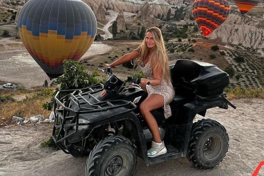 Una persona conduce un vehículo todo terreno en un entorno rocoso al aire libre, con globos aerostáticos al fondo. 1