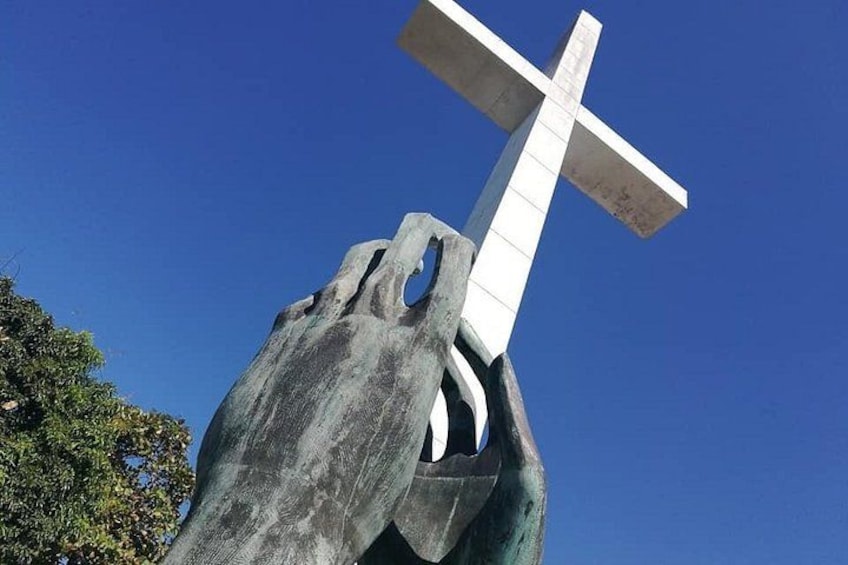 A large cross sculpture with a white cross on top, set against a clear blue sky. 3