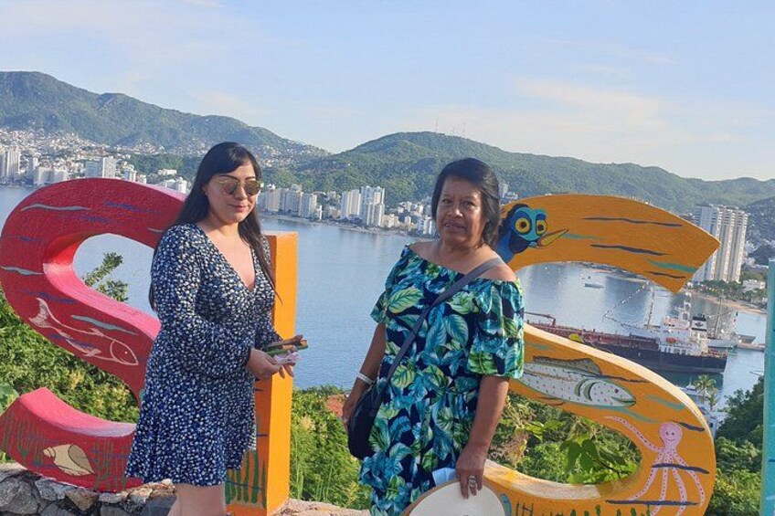 Two people standing in front of a large sculpture with a cityscape in the background. 2