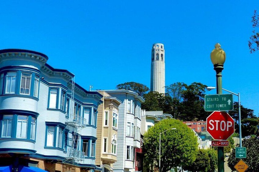 A street with Victorian-style houses, a stop sign, and a sign indicating stairs to Coli Tower. 2