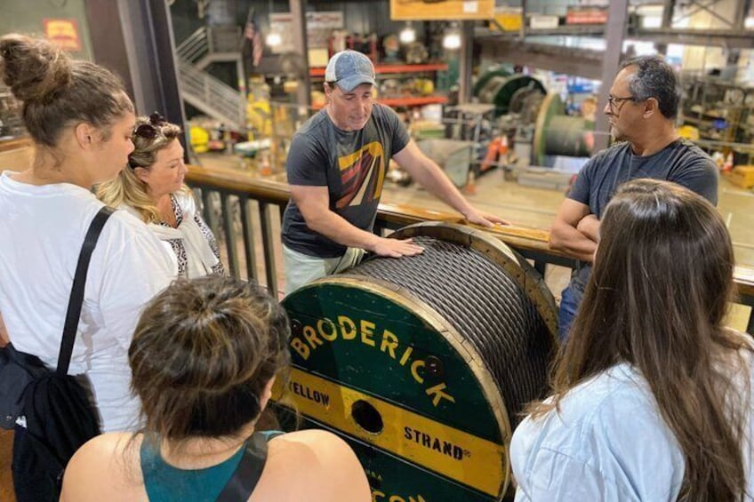A group of people observing a large spool of yellow and green wire labeled 'BRODERICK STRAND.' 4