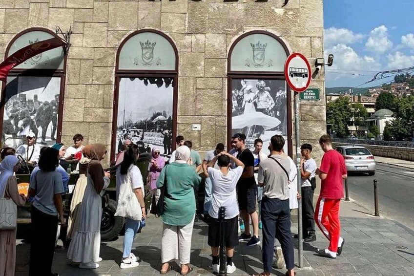 A group of people standing in front of a building with large arched windows and a coat of arms. 2