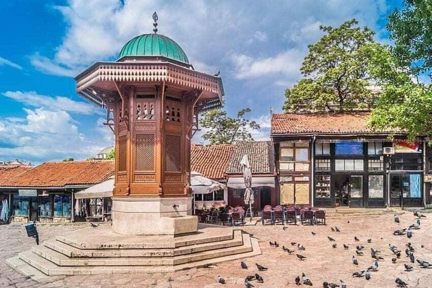 A gazebo with a green dome, a tiled plaza, and a building with a tiled roof. 4