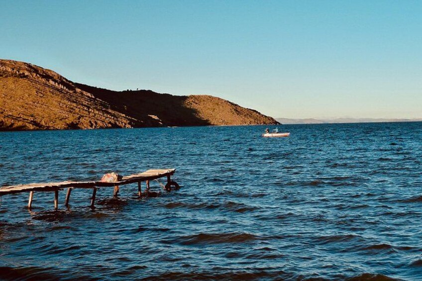 A wooden dock extending into calm water, a small boat in the distance, and a hilly landscape under a clear sky. 3