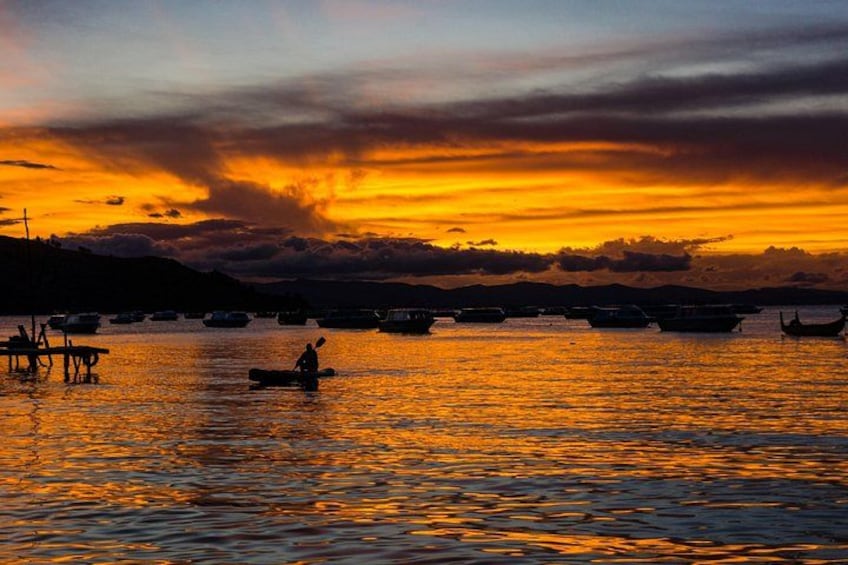 A sunset over a body of water with boats and a person rowing a boat. 1