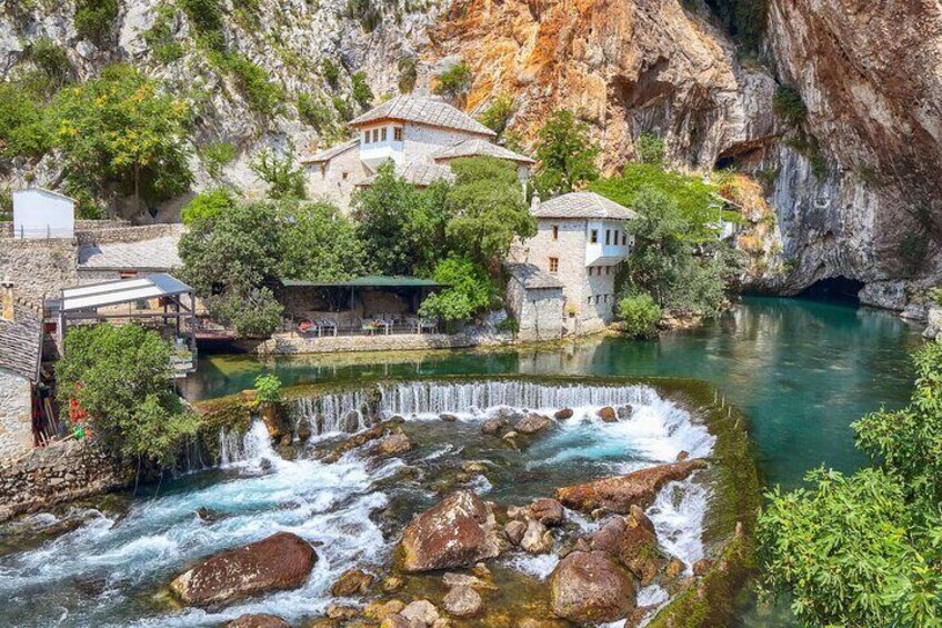 A river flowing through a rocky gorge with a waterfall, surrounded by buildings and greenery. 1