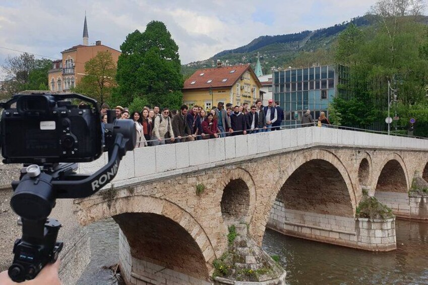 A stone bridge with arches, a group of people on it, and buildings in the background. 2