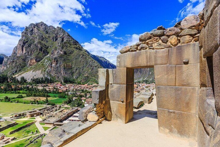 A stone structure with an archway, a mountainous landscape, and a town in the background. 3