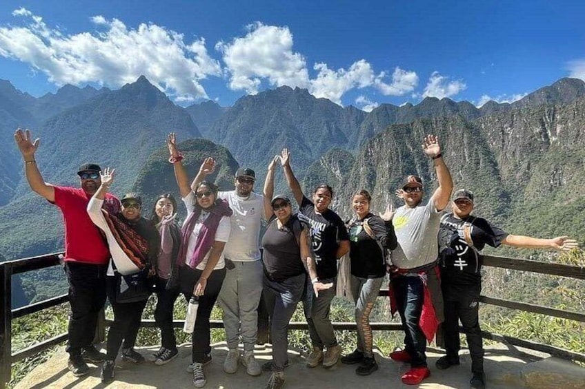 A group of people standing on a viewing platform with a mountainous landscape in the background. 2