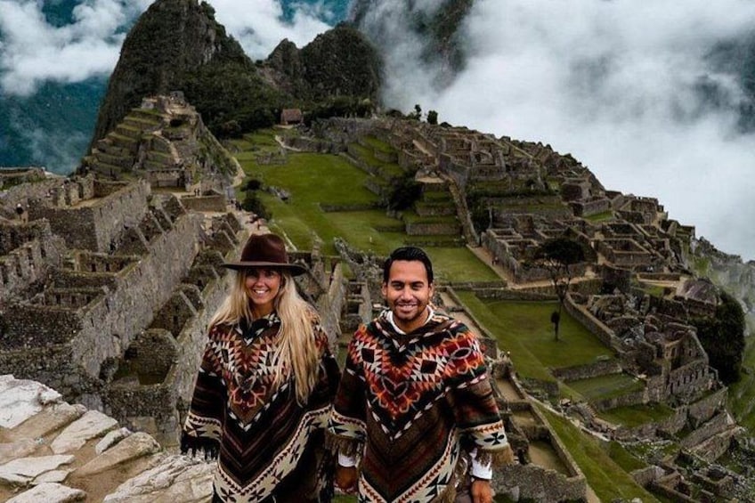 A couple standing in front of Machu Picchu with ancient ruins and mist in the background. 1
