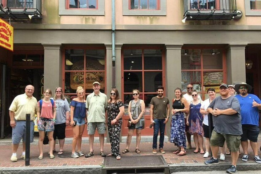 A group of people standing in front of a building with a sign that reads 'Cooking.' 2