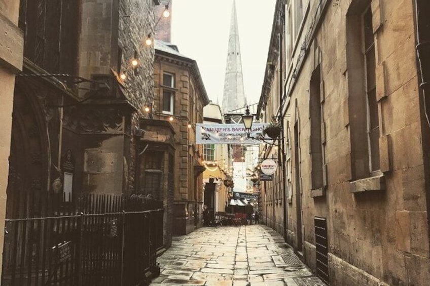 Une ruelle étroite pavée, bordée de bâtiments historiques, avec le clocher d’une église qui se profile au loin. 2