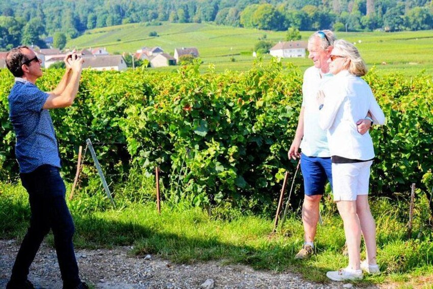 A person taking a photo, a vineyard, and a rural landscape with houses in the background. 5