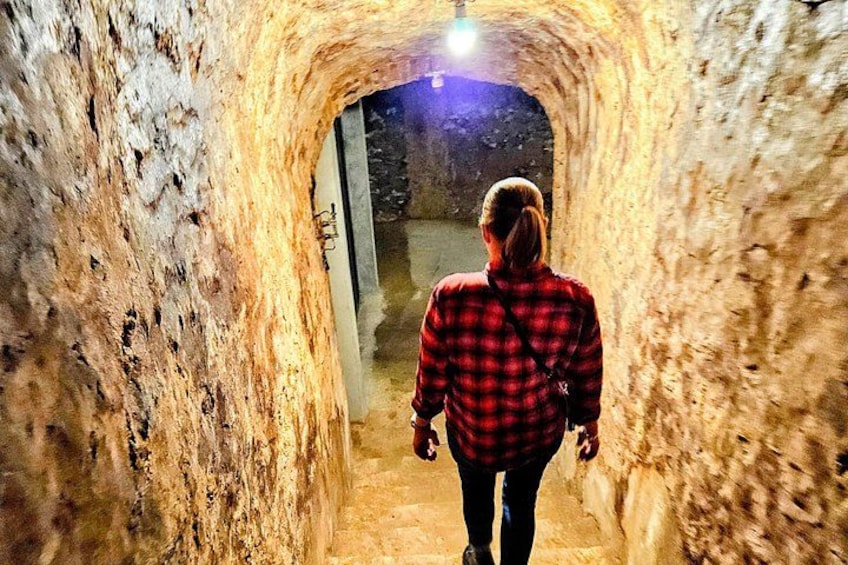 A person walking through a tunnel with rough walls and a light at the end. 4
