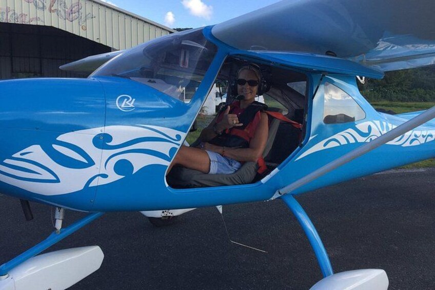 A small blue and white airplane parked on a tarmac with a person sitting inside. 2