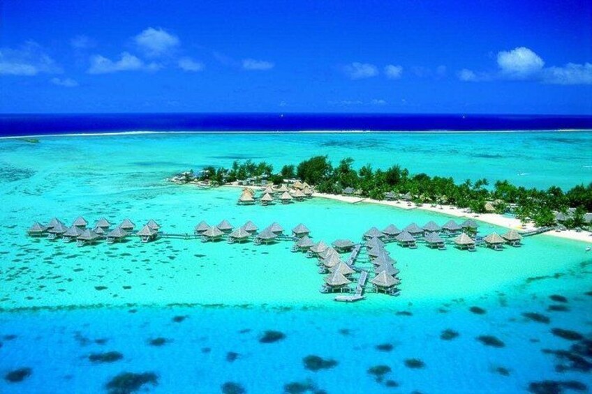 Vista aérea de una isla tropical con aguas turquesas cristalinas, bungalows sobre el agua y exuberante vegetación. 5
