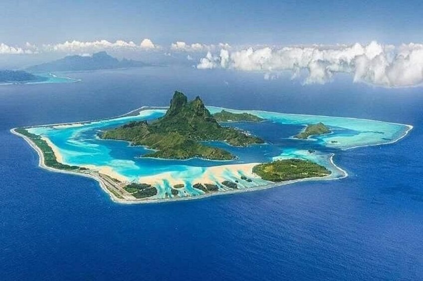 Vista aérea de una isla tropical con aguas azul turquesa, un pico central y islas más pequeñas alrededor. 4