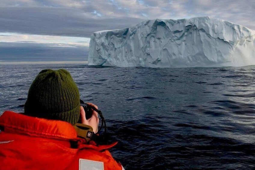 Una persona con chaqueta roja fotografiando un iceberg en el océano. 3