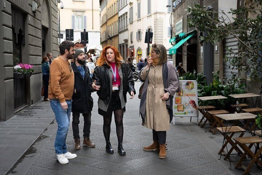 A group of people standing on a city street with buildings and outdoor seating areas. 1