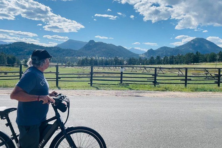 A person standing next to a bicycle on a road with a mountain landscape in the background. 4