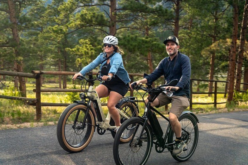 Two people riding bicycles on a paved path surrounded by trees. 2