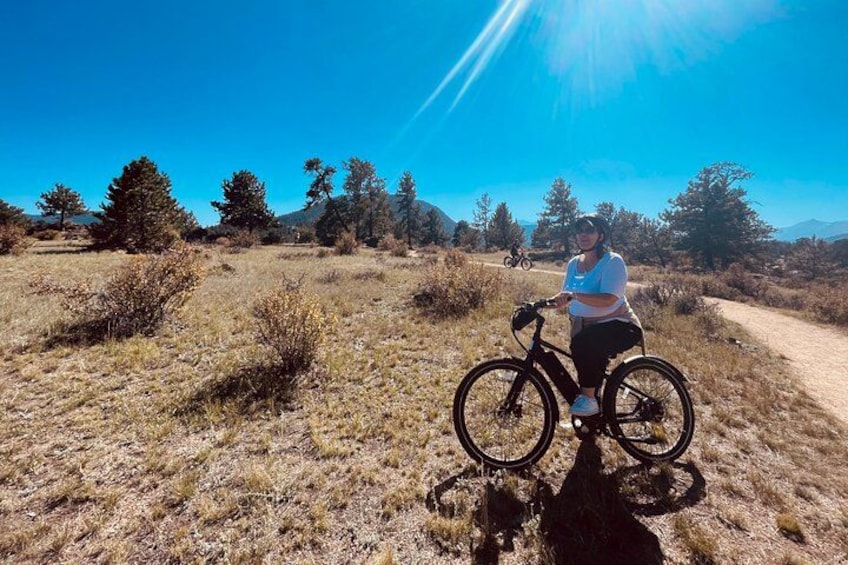A person on a bicycle on a dirt path with dry grass and trees in the background. 4