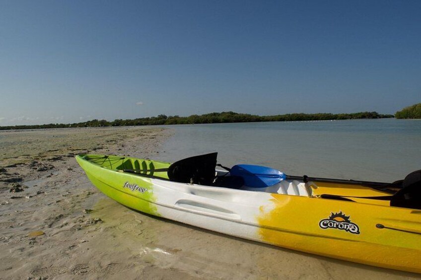 A kayak with a green and yellow design on a sandy beach by a calm body of water. 5