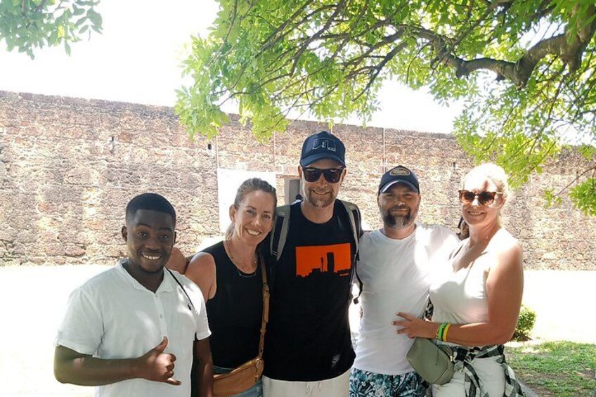 A group of people standing outdoors with a stone wall and trees in the background. 1