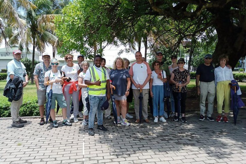 A group of people standing outdoors, some wearing safety vests, under a large tree. 2