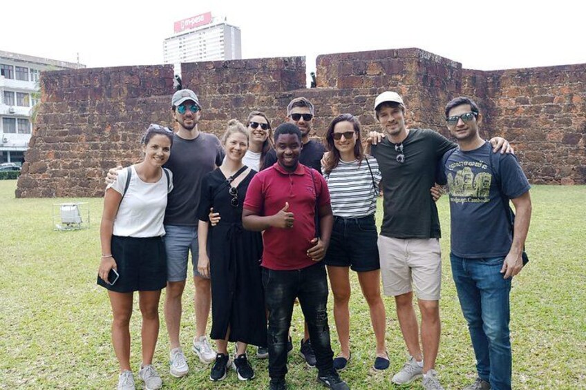 A group of people standing in front of a stone wall with a building in the background. 1