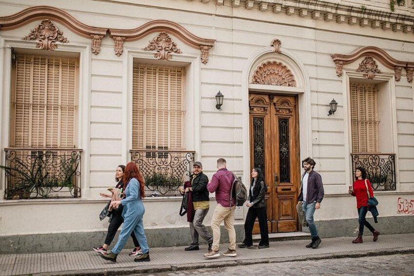 Un grupo de personas caminando por una calle con edificios ornamentados y una puerta de madera grande. 2