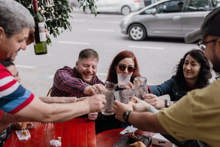 Eine Gruppe von Personen erhebt beim Tisch im Freien die Gläser. 2