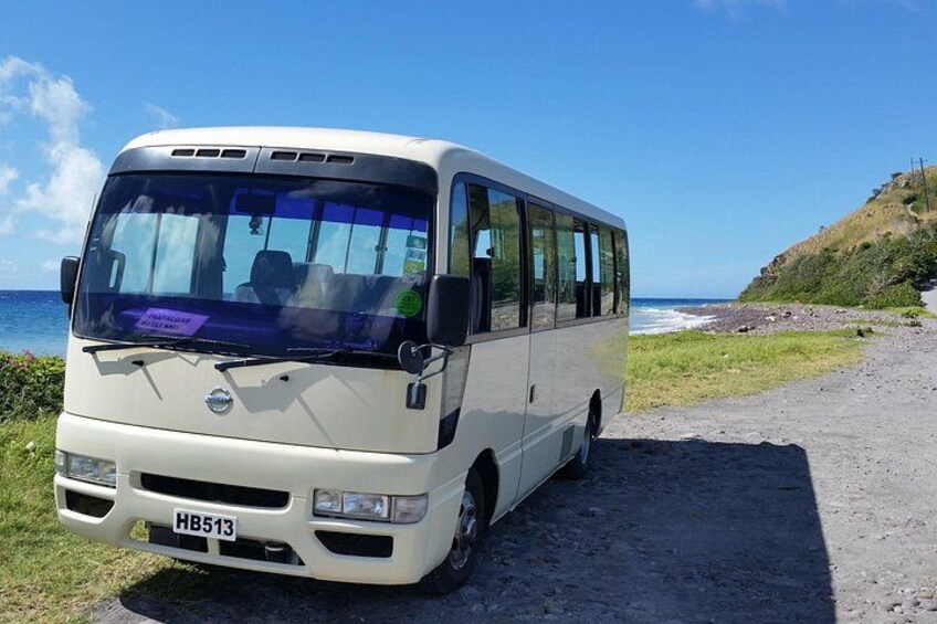 A white bus parked on a gravel path by the ocean. 2