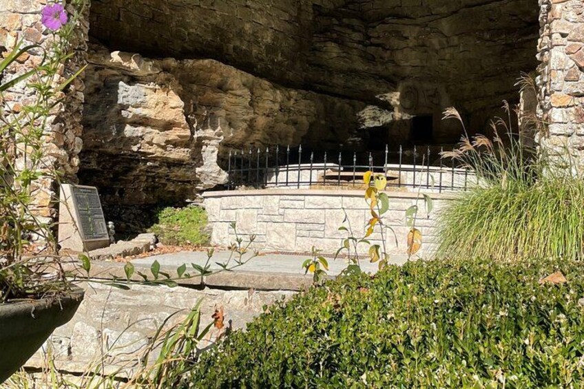 L’entrée d’une grotte, avec un banc en pierre, une rambarde en métal et un panneau indicateur. 1
