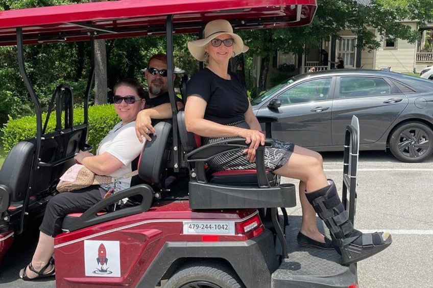 Une voiturette de golf rouge, avec trois passagers à bord, est garée sur un parking. 3