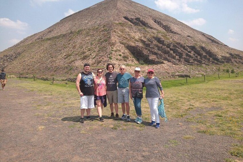 A group of people standing in front of a large hill or mound. 1