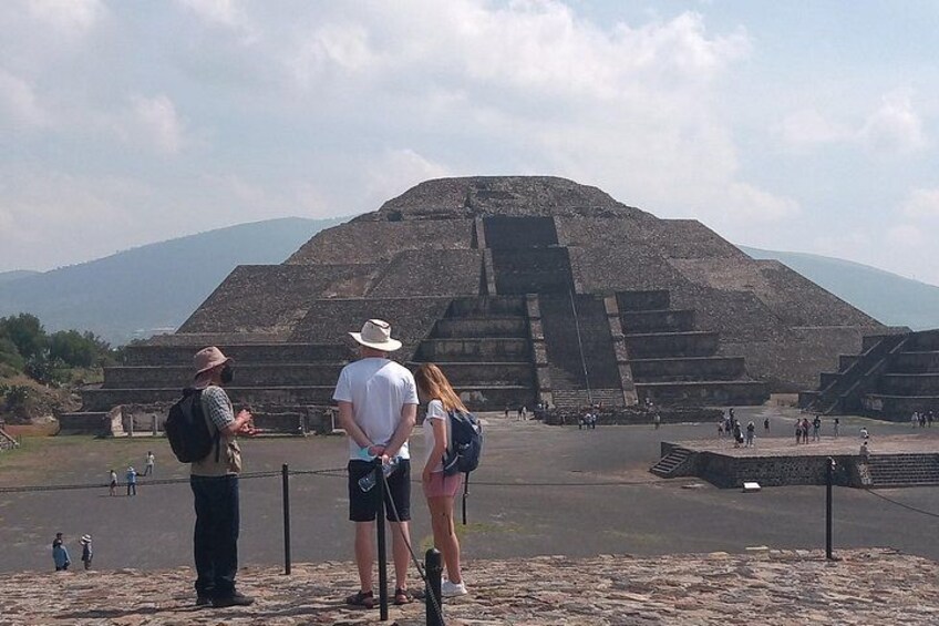A large pyramid structure with tourists observing it. 1