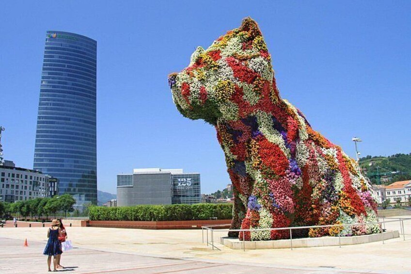 Una grande scultura floreale a forma di orso in una piazza cittadina, con moderni edifici sullo sfondo. 1