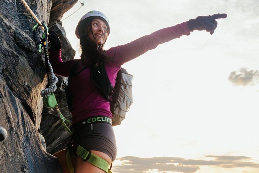 A person climbing a rock face with a helmet, harness, and pointing towards the sky. 3