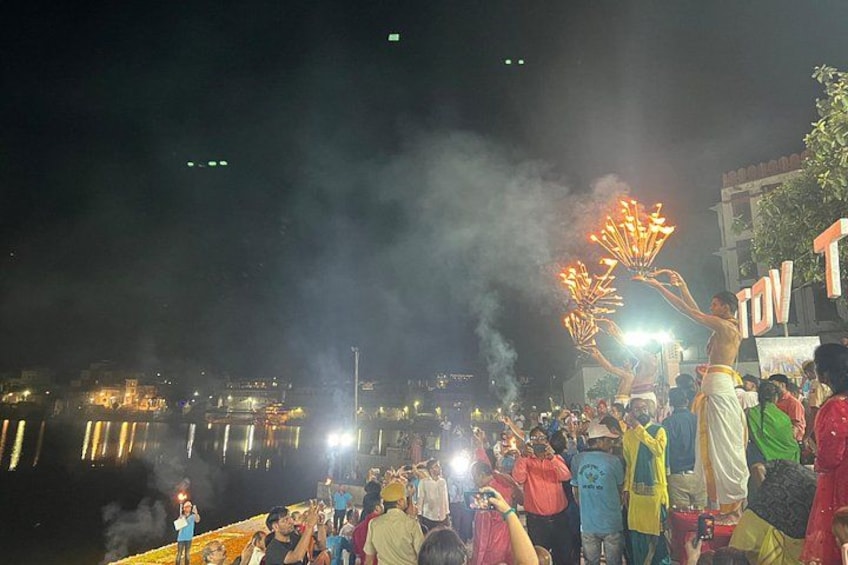 A nighttime outdoor gathering with people holding lit torches, a crowd, and a body of water in the background. 2