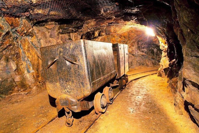 A mining truck in a tunnel with rocky walls and a light source at the end. 3
