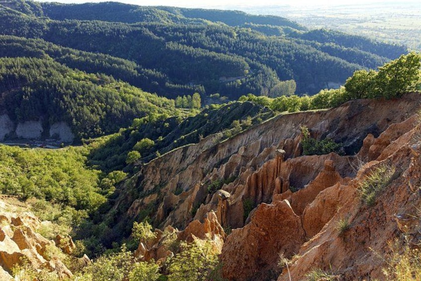 A mountainous landscape with a winding road, rocky cliffs, and dense forest. 2
