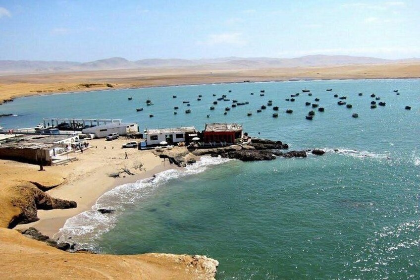 Une zone côtière avec une plage de sable, un petit village avec des bâtiments et une vaste étendue d’eau où se trouvent de nombreux bateaux. 2
