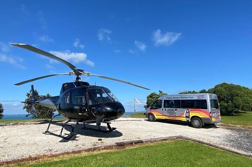 A black helicopter and a colorful bus parked on a gravel area with a clear blue sky. 4