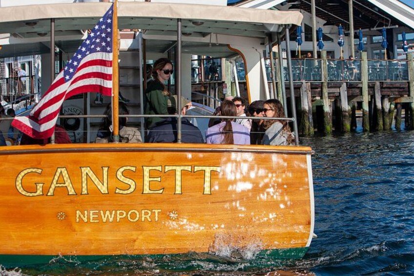 A wooden boat named Gansett Newport with passengers and an American flag. 5