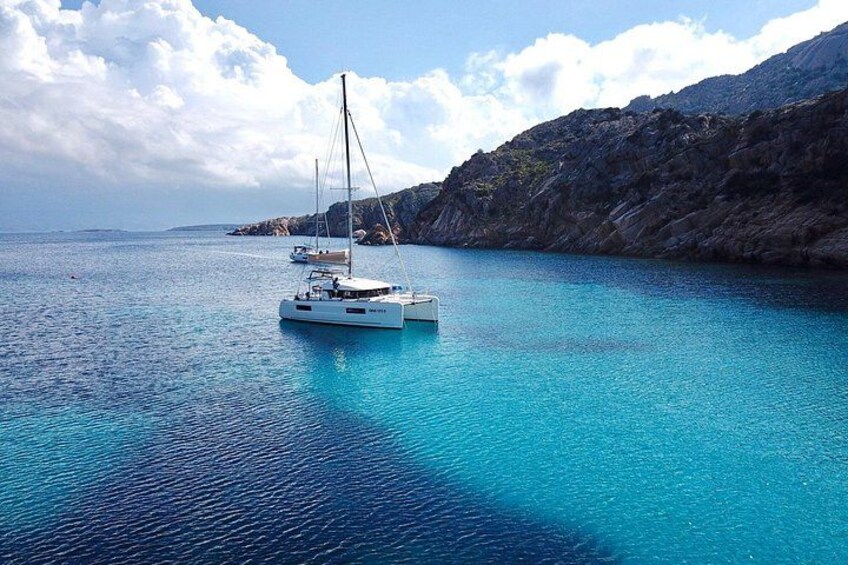 Een witte zeilboot op turquoise water, met rotsachtige kliffen op de achtergrond. 5