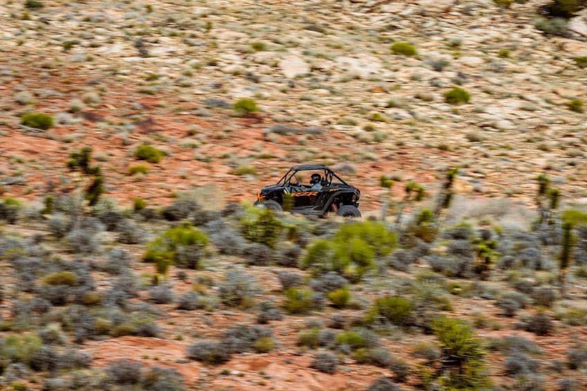 Un véhicule traverse un paysage désertique, caractérisé par une végétation clairsemée et un terrain rocheux. 3
