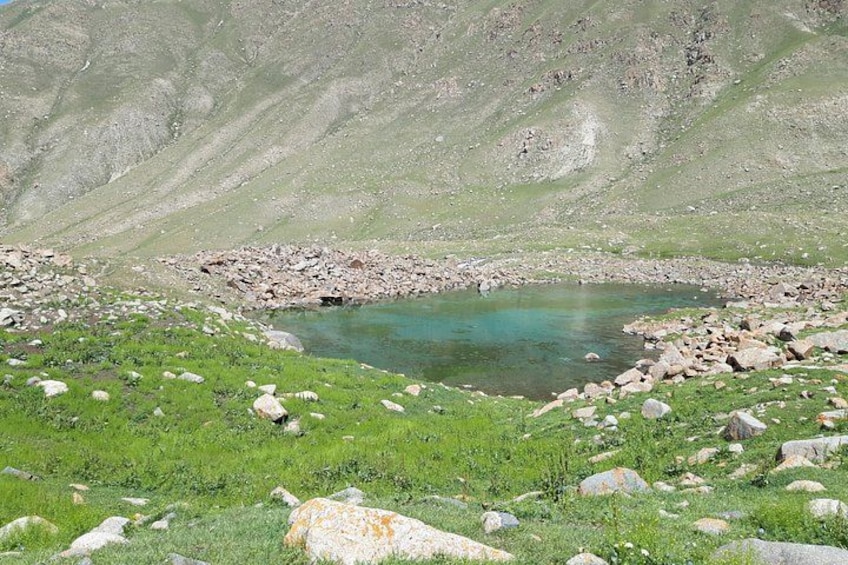 Paisaje montañoso con un pequeño lago turquesa rodeado de terreno rocoso y vegetación escasa. 2