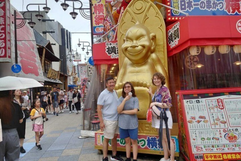 A street with a large golden statue, a food stall, and people walking. 4